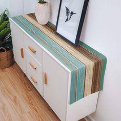 a white cabinet with two pictures on top and some plants in the corner next to it