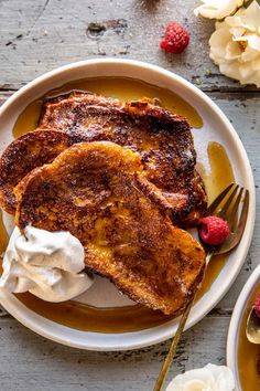 french toast with whipped cream and raspberries on a white plate next to flowers