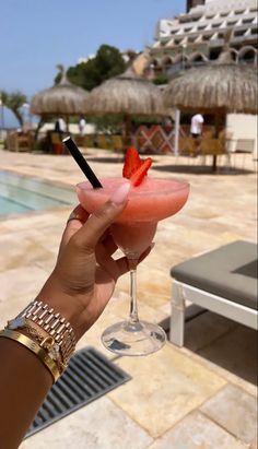 a person holding up a drink in front of a swimming pool