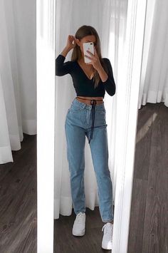 a woman taking a selfie in front of a mirror wearing high waist jeans and white sneakers