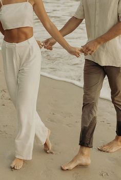 a man and woman holding hands on the beach