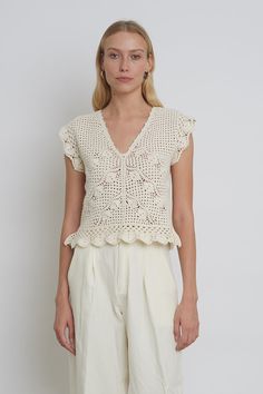 a woman standing in front of a white wall wearing a top with crochet