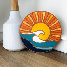 an orange and blue plate sitting on top of a wooden floor next to a white vase