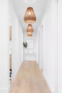 a long white hallway with wood flooring and hanging lights