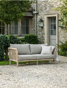 a couch sitting on top of a gravel covered field next to a stone building and trees