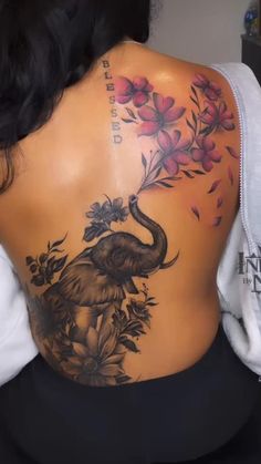 the back of a woman's body with an elephant and flowers tattoo on it