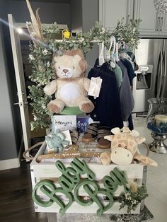 a teddy bear sitting on top of a wooden crate filled with baby clothes and other items