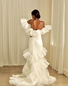 the back of a woman in a white wedding dress with ruffles on it