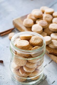 a glass jar filled with cookies on top of a wooden cutting board next to cinnamon sticks