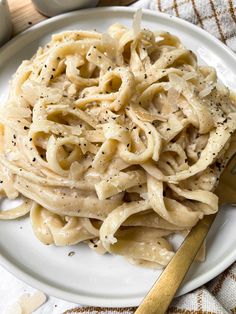 a white plate topped with pasta covered in sauce and seasoning next to a fork