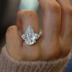 a close up of a person's hand holding an engagement ring with two pear shaped diamonds