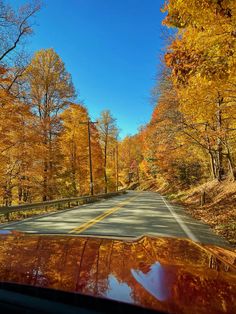 a car driving down a road surrounded by trees in the fall season with orange and yellow leaves