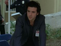 a man in a suit and tie sitting on a blue chair next to a police officer