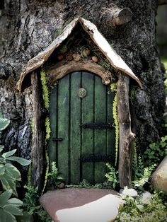 a green fairy door in the middle of a tree trunk with moss growing on it