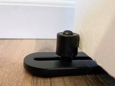 a black object is sitting on the floor next to a white wall and wooden floor