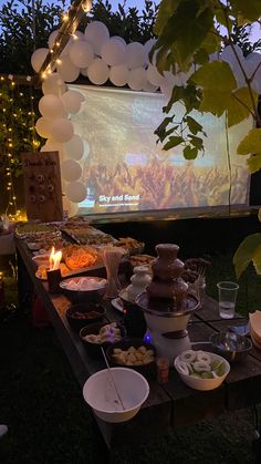 an outdoor movie screen is set up with food and drinks in front of the screen