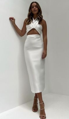 a woman standing in front of a white wall wearing a skirt and cropped top