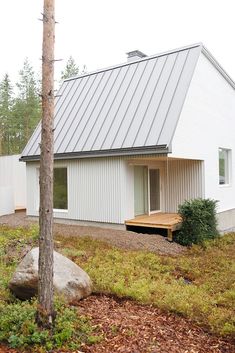 a white house with a metal roof and wooden deck in the grass next to a tree