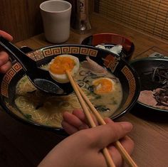 someone holding chopsticks over a bowl of ramen with an egg in it