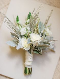 a bridal bouquet with white flowers and greenery on a piece of parchment paper