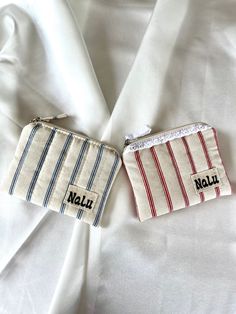 two small zippered pouches sitting on top of a white cloth covered bed sheet