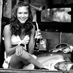 a black and white photo of a woman sitting in the back of a car holding a drink