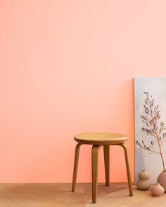 a small wooden stool next to a pink wall