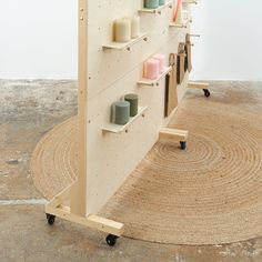 a wooden shelf with candles on it in front of a white wall and round rug