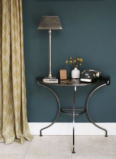 a small table with a lamp on it in front of a blue wall and gold curtains