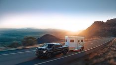 a truck towing a camper on the side of a road with mountains in the background