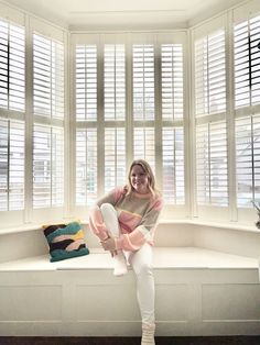 a woman sitting on a window sill in front of a large window with shutters