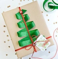 a present wrapped in green paper with a red ribbon on it next to a christmas tree ornament