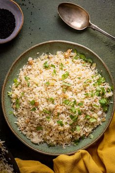 a bowl filled with rice and green onions next to two spoons on a table