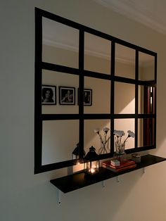 a mirror is hanging on the wall above a shelf with candles and flowers in it