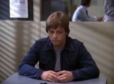 a young man sitting at a table with his hands on his chest and looking to the side