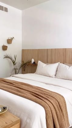 a bed with white linens and pillows in a bedroom next to potted plants