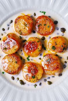 a white plate topped with sliced tomatoes covered in sauce and garnished with capers