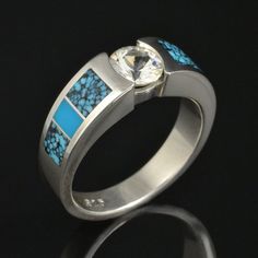 a silver ring with blue stones and a diamond in the center on a black background