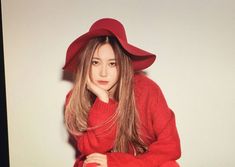 a woman in a red sweater and hat poses for a photo with her hand on her chin