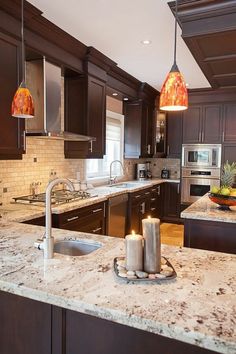 a kitchen with marble counter tops and dark wood cabinets is lit by two candles on the island