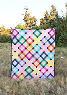 a multicolored quilt sitting on top of a grass covered field