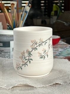 a white vase sitting on top of a table next to paintbrushes and pencils