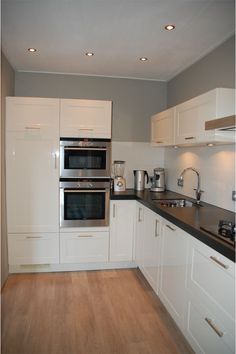 a kitchen with white cabinets and black counter tops is pictured in this image, there are two ovens on each side of the wall