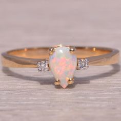 an opal and diamond ring sitting on top of a wooden table