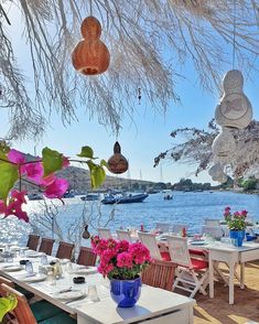 an outdoor dining area with tables and chairs near the water, surrounded by hanging flowers