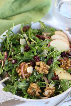 a salad with apples, walnuts and cranberries in a white bowl on a table