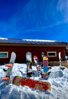 there are many snowboards in the snow by a building with a red roof and blue sky