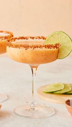 two margaritas sitting on top of a table with lime slices