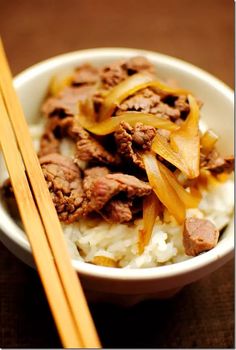 a bowl filled with rice and meat next to chopsticks