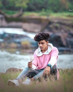 a young man sitting in tall grass next to a river